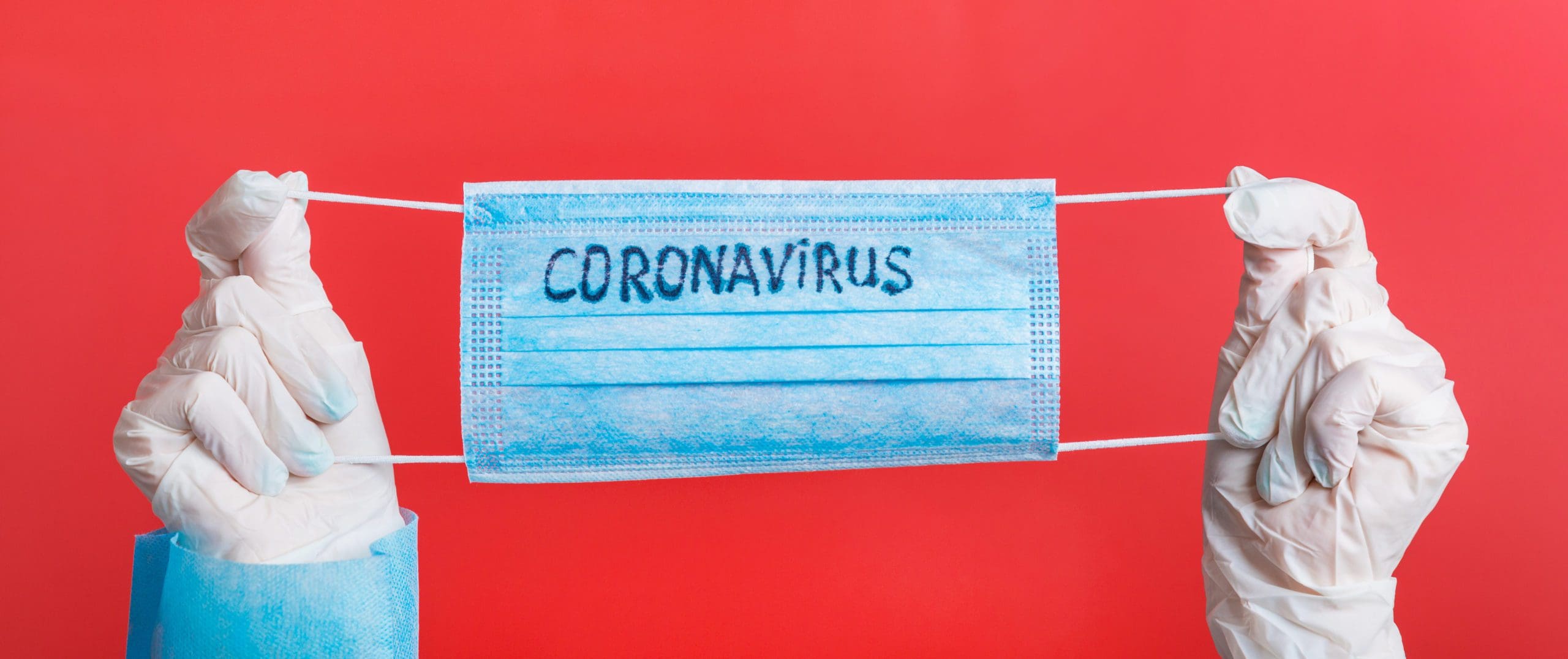 Female hands in medical gloves holding protective mask with coronavirus text on it at red background. Health care concept. Coronavirus concept.