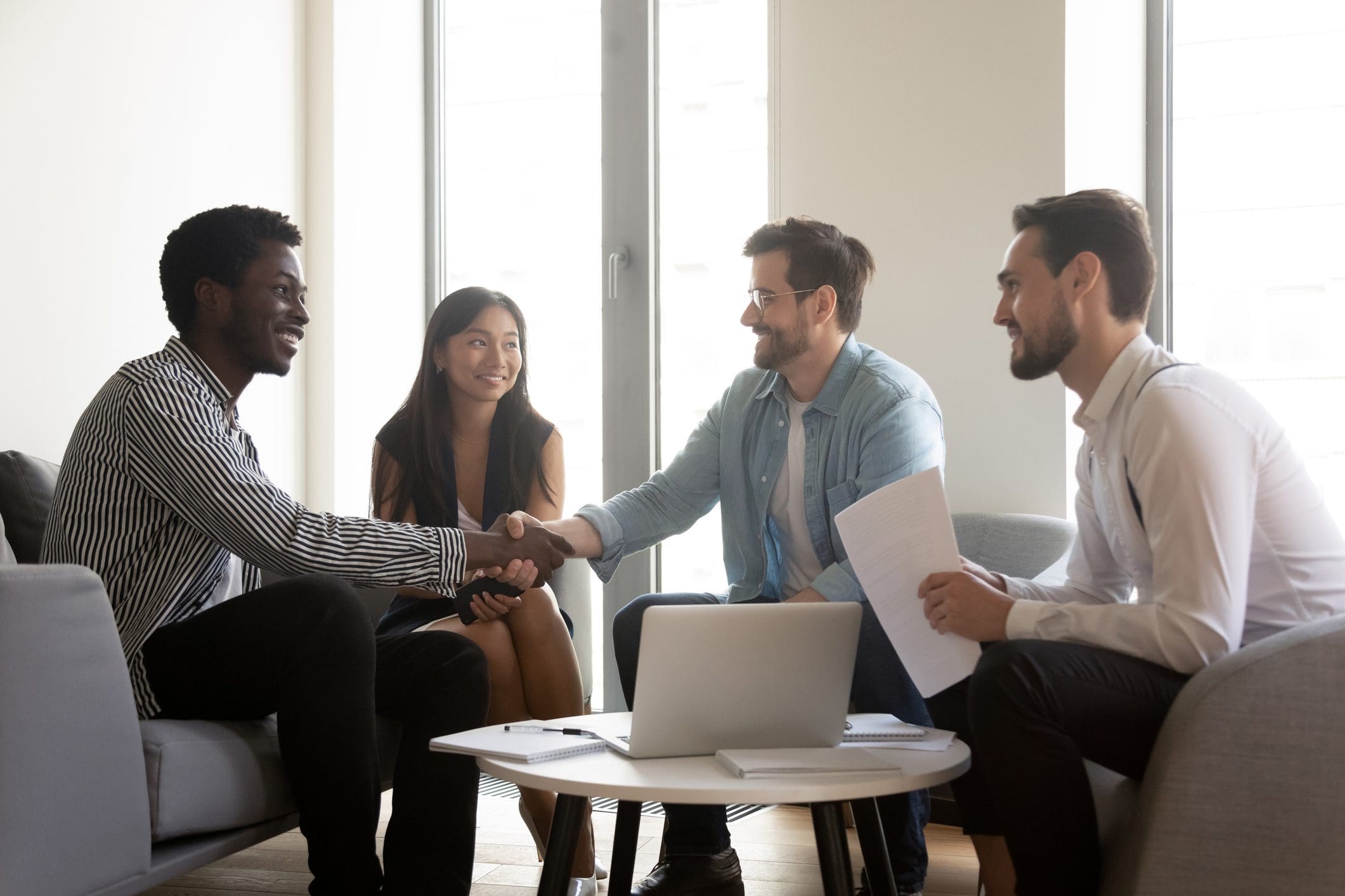Smiling diverse male company representatives colleagues or manager and client handshaking at multiethnic group meeting expressing respect make financial business deal thank for good teamwork result