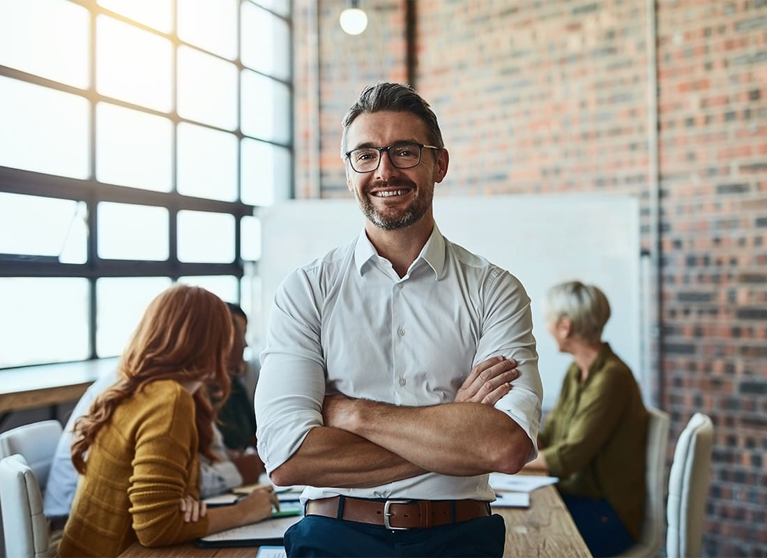 Business Insurance - Portrait of a Cheerful Middle Aged Businessman Standing in Front of a Conference Table During a Meeting with his Arms Folded