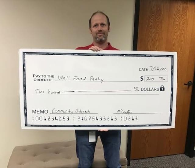 Social Responsibility - Smiling Middle Aged Man Holding a Large Check for the Well Food Pantry