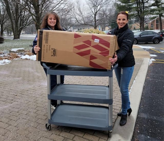 Social Responsibility - Two Smiling McConkey Female Employees Holding a Large Box During the McConkey Box Project Event