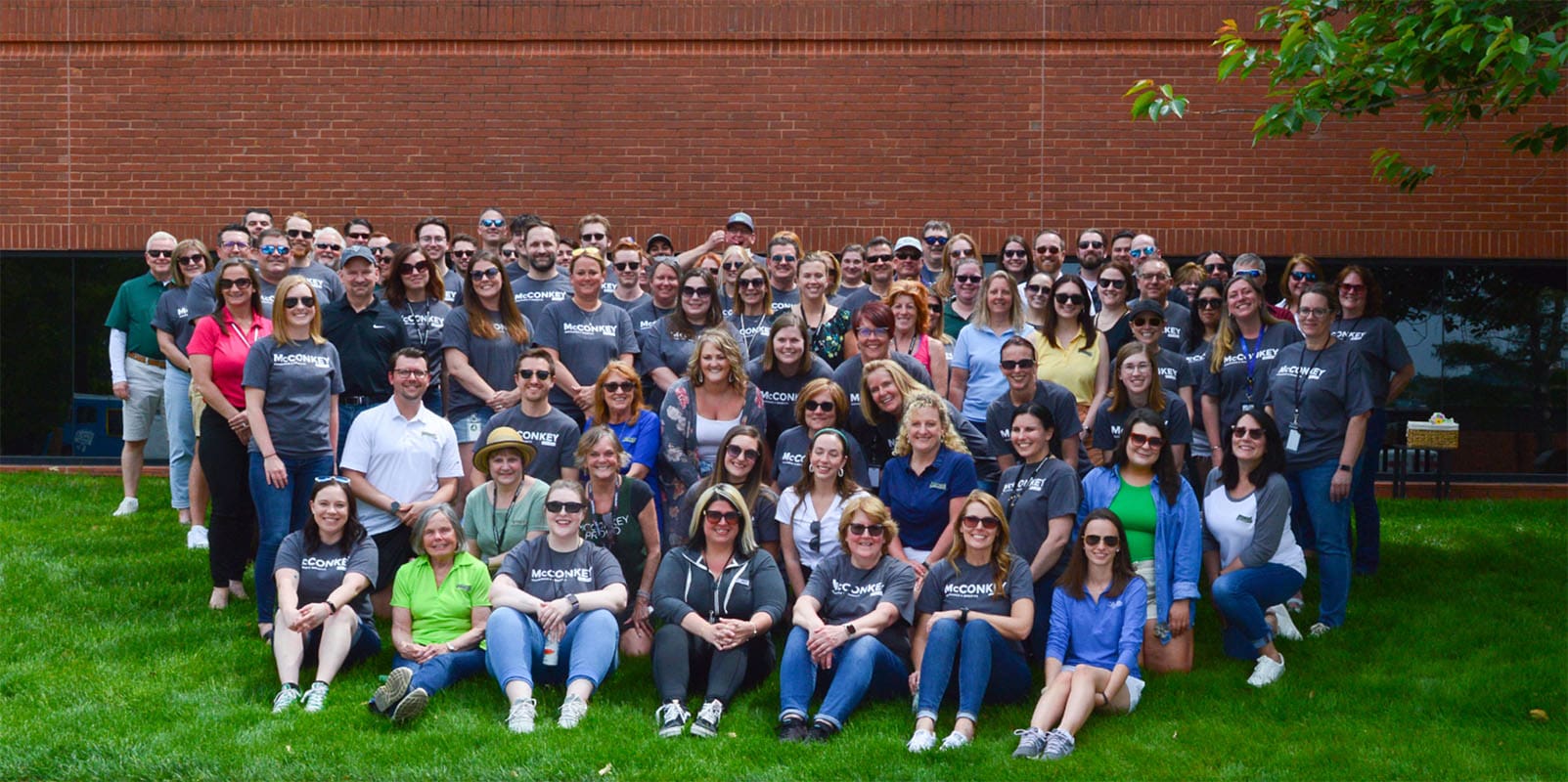 Careers - Portrait of Large Group of Smiling McConkey Employees Standing and Sitting on the Green Grass Outside the McConkey Building on a Sunny Day