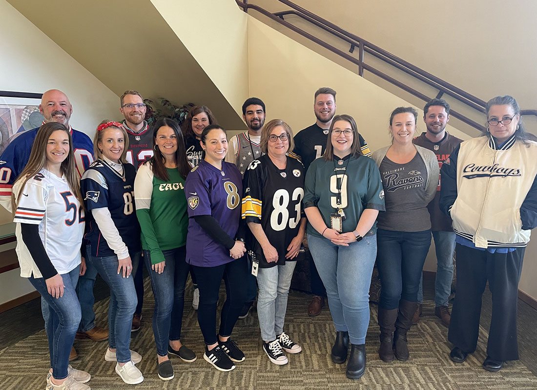 We Are Independent - Portrait of Smiling McConkey Insurance Team Members Standing Inside the Office Next to a Staircase Wearing Sports Jerseys