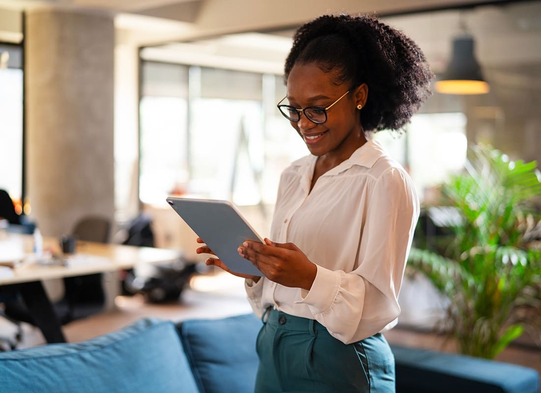 FAQs - Portrait of a Cheerful Young African American Business Woman Standing in the Office While Looking at a Tablet in her Hands